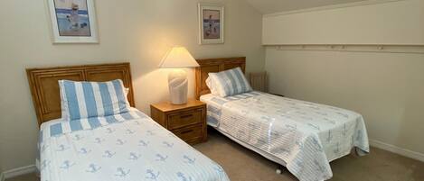 Een slaapkamer met twee eenpersoonsbedden, een plafondventilator en een nachtkastje met een lamp.