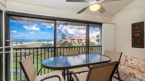 A balcony with a glass table and chairs, a ceiling fan, and a view of the ocean and buildings. - Cresent Beach Gulf view 2Bd/2Ba Condo (Sarasota)