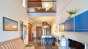 Una sala moderna con un sofá, un comedor con sillas azules, una cocina con armarios azules y una escalera que sube a un nivel superior.