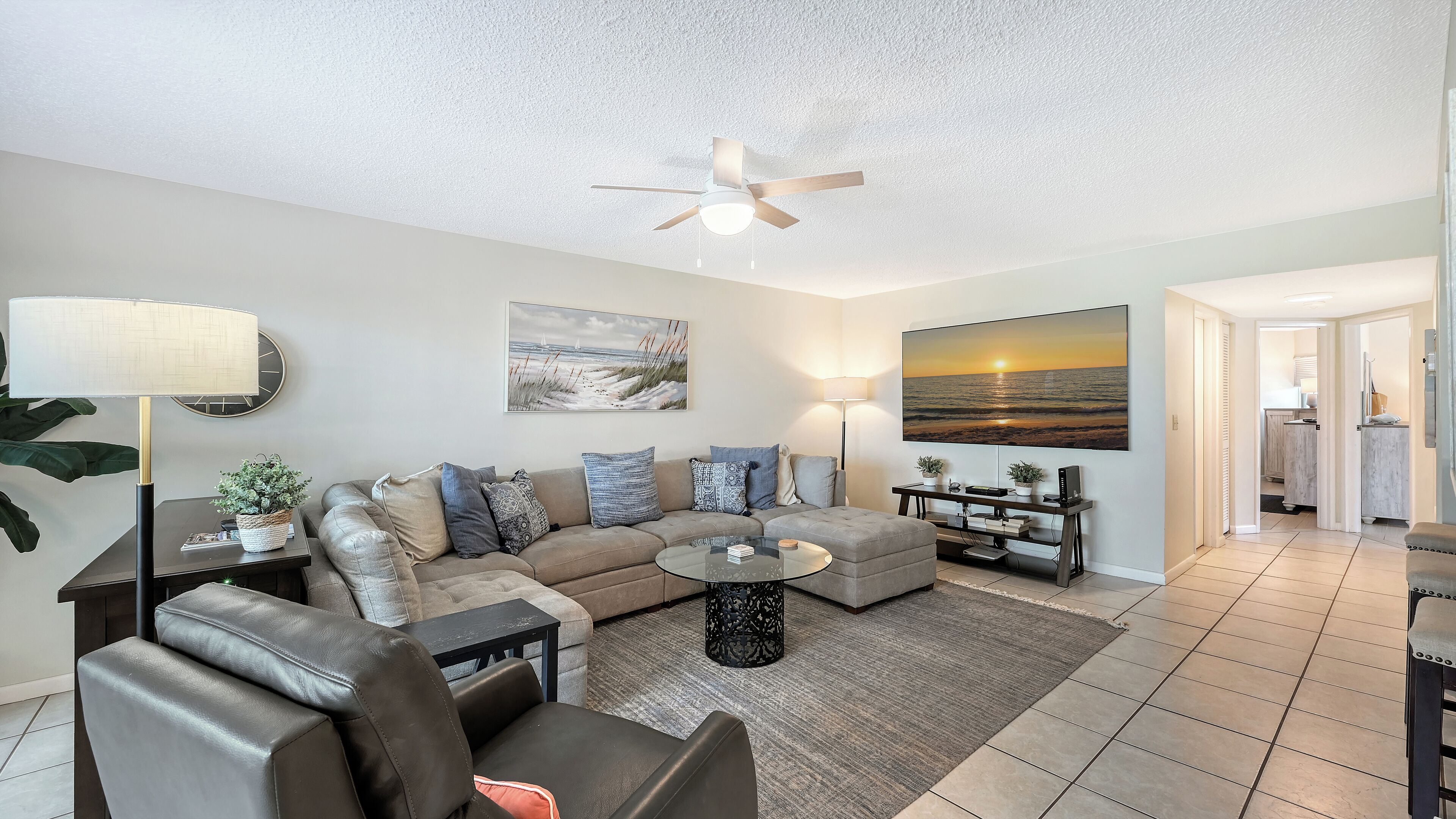 A modern living room with a sectional sofa, a glass coffee table, and a ceiling fan.