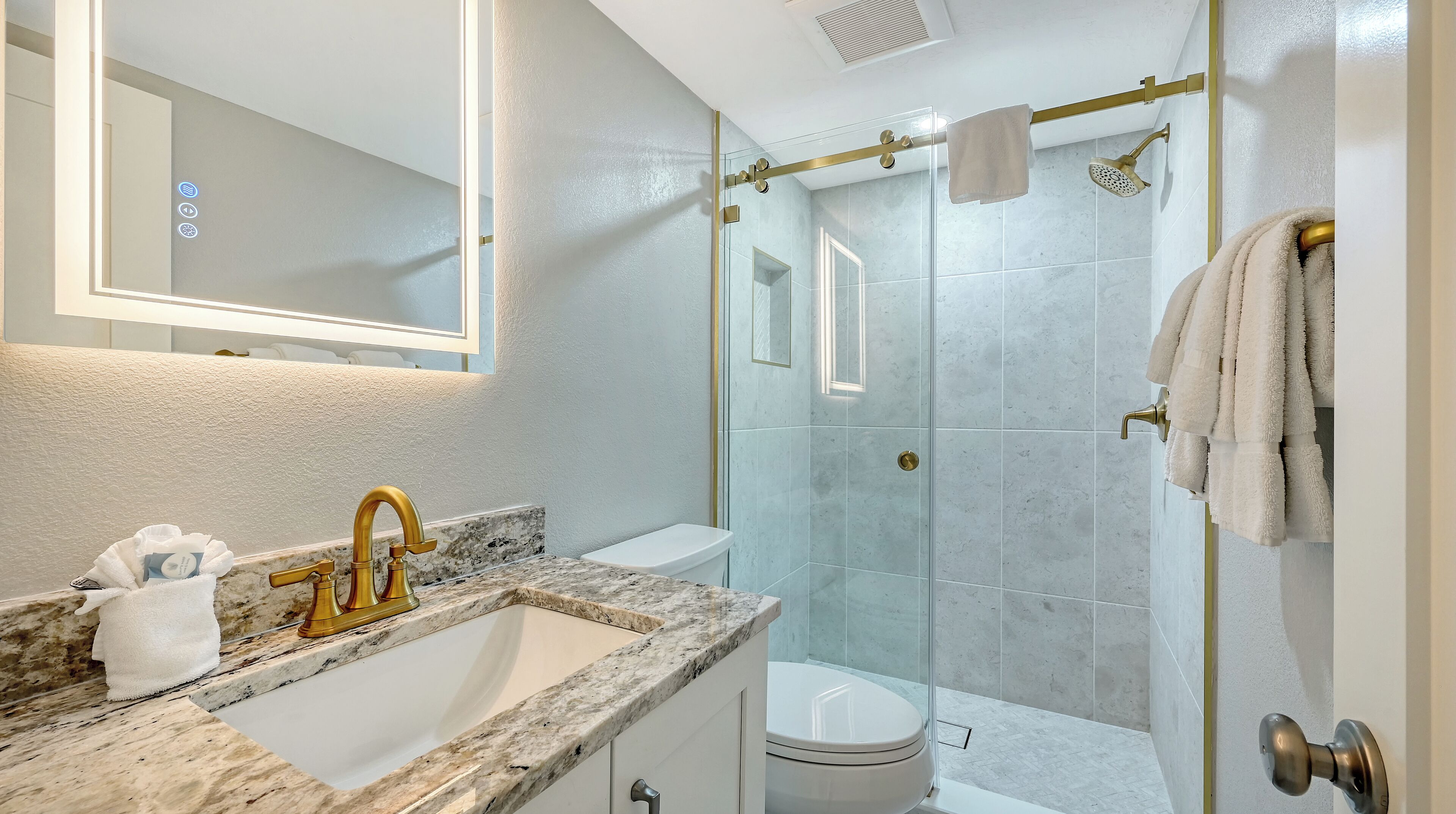 Une salle de bain avec un lavabo en marbre, des toilettes et une douche séparée par une paroi en verre.