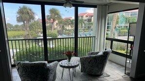 A balcony with two patterned armchairs, a small round table with a vase of flowers, and a view of a landscaped area with palm trees and buildings. - Spectacular view on Crescent beach (Sarasota)