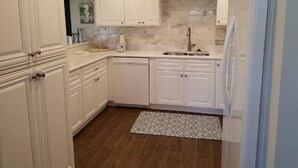 A kitchen with white cabinetry, a marble backsplash, a stainless steel sink, and a dishwasher. - Spectacular view on Crescent beach (Sarasota)