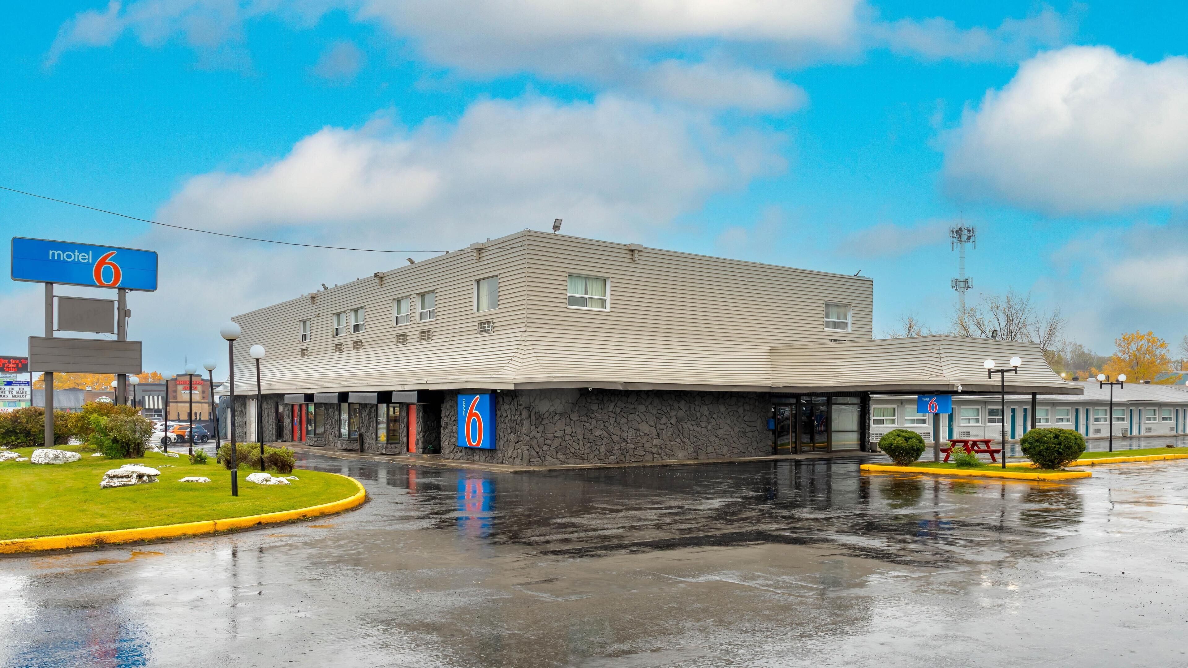 Un motel à la façade en pierre, doté de nombreuses fenêtres et d’un parking.