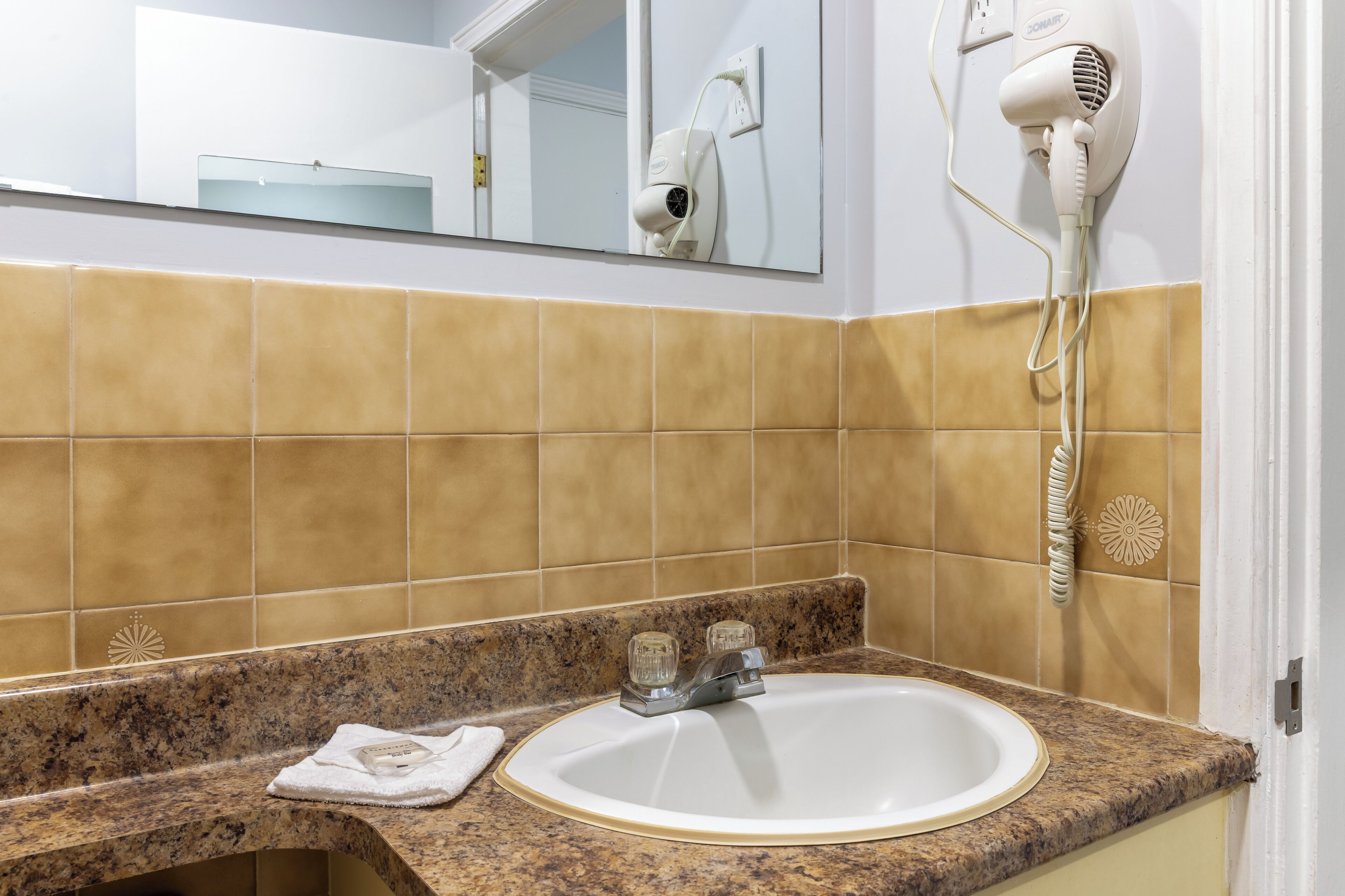 A bathroom with a sink, mirror, and hairdryer mounted on the wall.