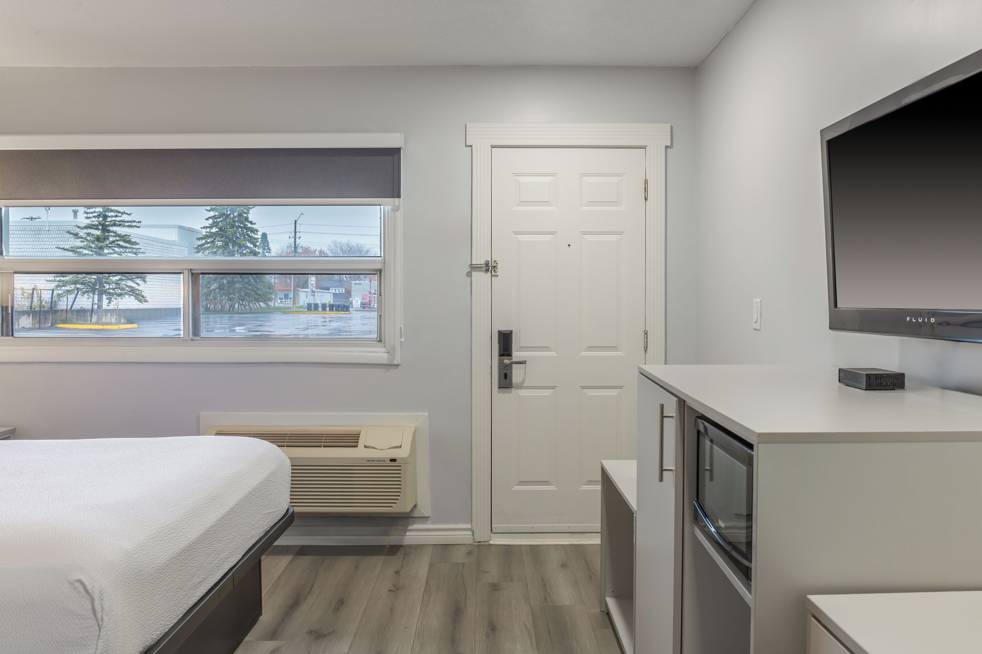 A bedroom with a bed, a window, a door, and a TV.