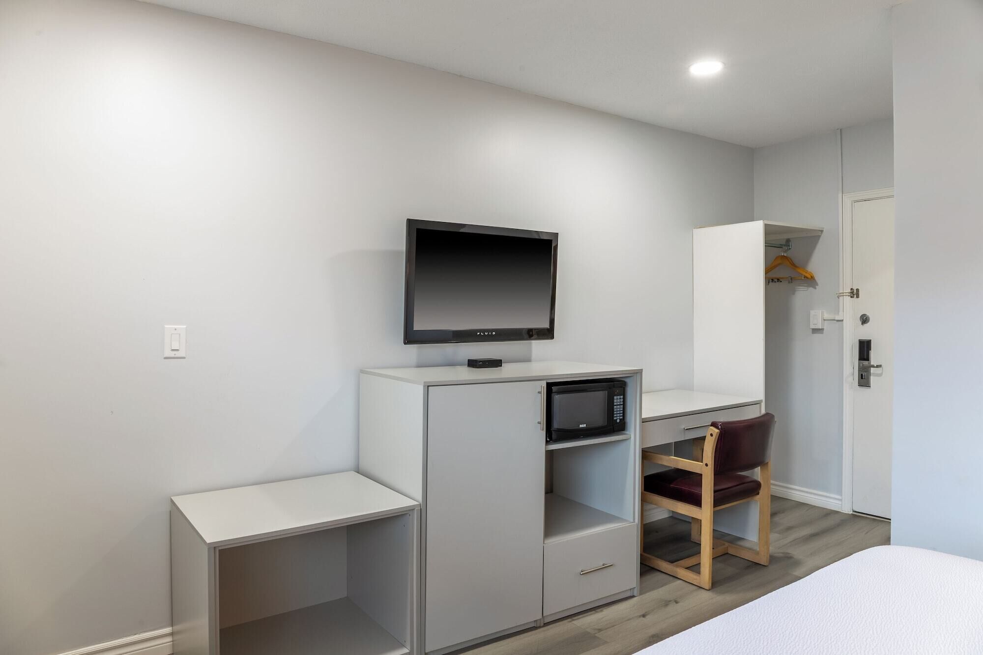Un dormitorio moderno con una cama, un escritorio con televisor de pantalla plana, un microondas y una silla.