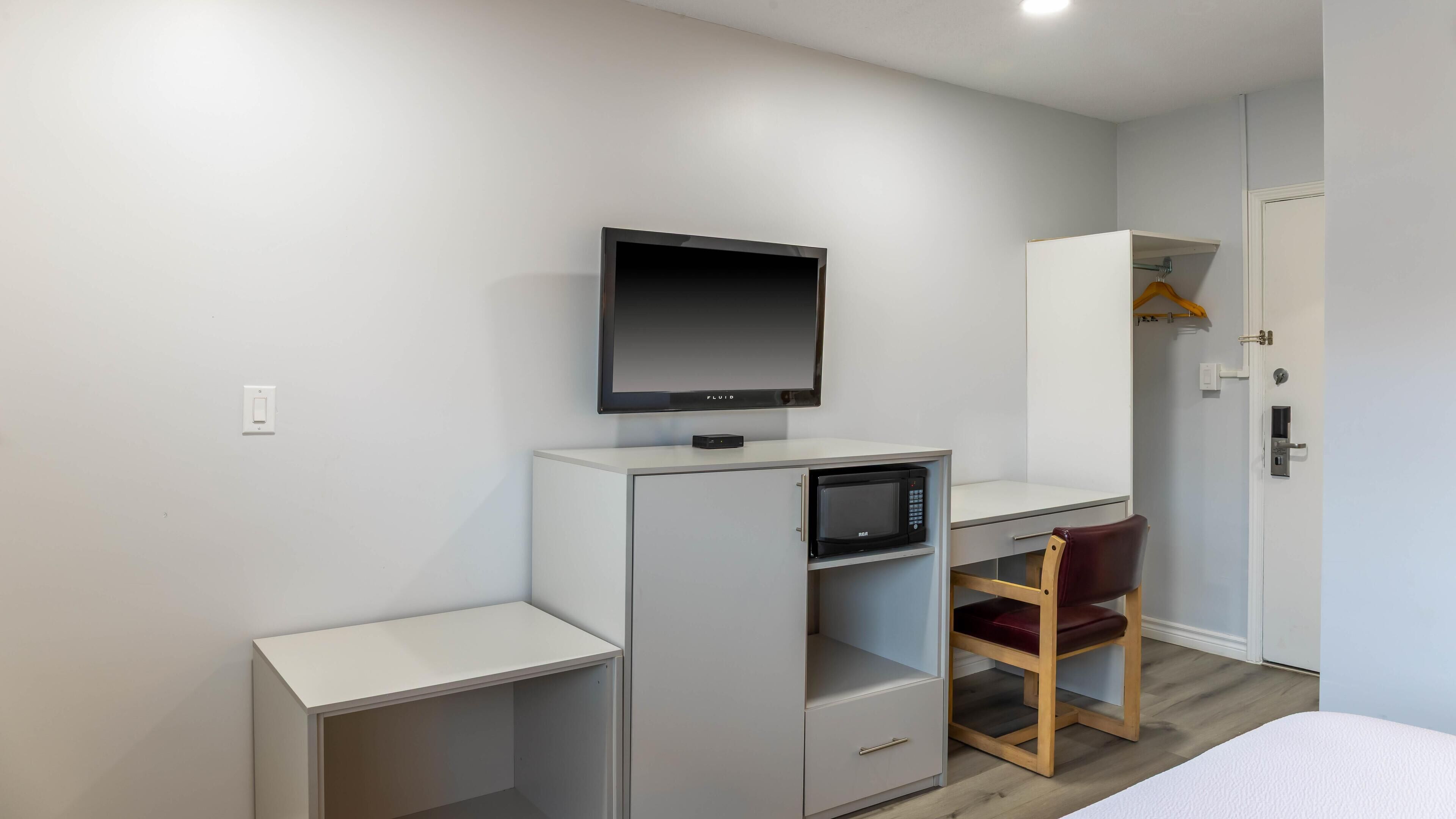 Una habitación compacta con escritorio, televisor, microondas, armario y una silla.