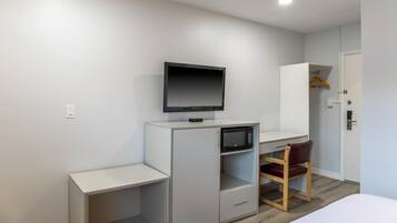 Una habitación compacta con escritorio, televisor, microondas, armario y una silla.