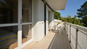 A balcony with a white railing, a small table with chairs, and a sliding glass door leading to a room.