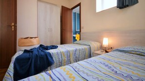 Ein Hotelzimmer mit zwei Betten, einem Kleiderschrank, einem Fenster mit Vorhängen und einer Nachttischlampe.
