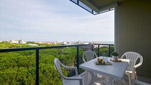 Un balcon avec une table et des chaises, offrant une vue sur un paysage verdoyant et sur les contours d’une ville lointaine.