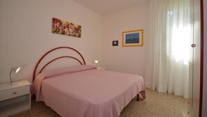 Ein Schlafzimmer mit einem Einzelbett, einem Nachttisch mit Lampe, einem Fenster mit Vorhängen und einem Wandbild.