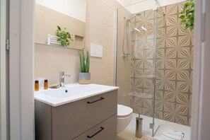 A modern bathroom with a glass shower enclosure, a white sink with a beige cabinet, and a potted plant. - Corte Nicolaiana Apts by Wonderful Italy (Bari)