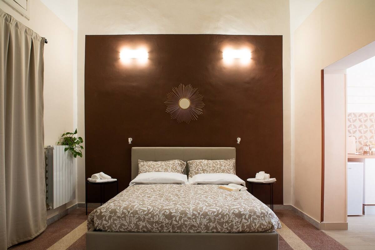 A neatly arranged hotel room with a large bed, two bedside tables, a wall-mounted light fixture, and a radiator.