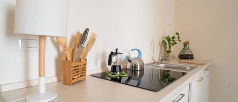 Een keuken met een aanrecht, een spoelbak, een waterkoker, een koffiezetapparaat, een plant en een houder voor keukengerei.
