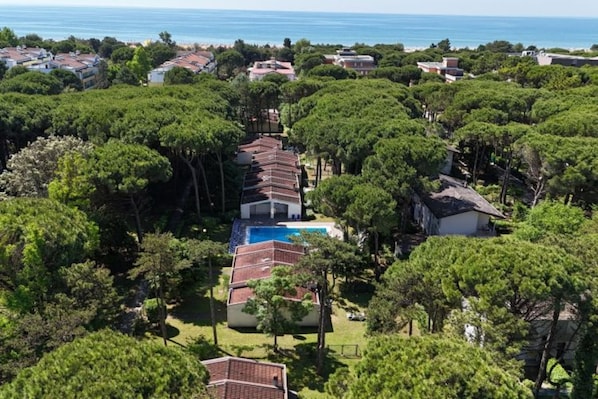 Una propiedad costera con una fila de villas, una piscina central y árboles densos que la rodean.