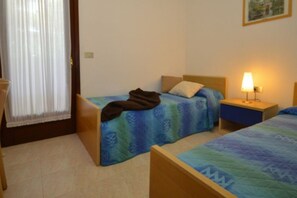 Une chambre d’hôtel avec deux lits simples, une table de chevet avec une lampe et une fenêtre avec des rideaux.