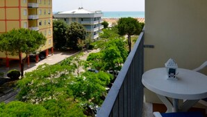 Un balcon donnant sur une plage, un immeuble à la façade rouge et jaune, et une table blanche agrémentée d’un petit objet décoratif.