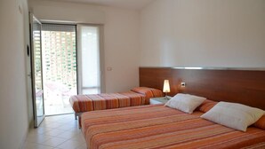 A hotel room with two beds, a wooden headboard, a nightstand with a lamp, and a sliding glass door leading to an outdoor area. - Charming apartment with balcony and shared pool (Bibione Pineda)