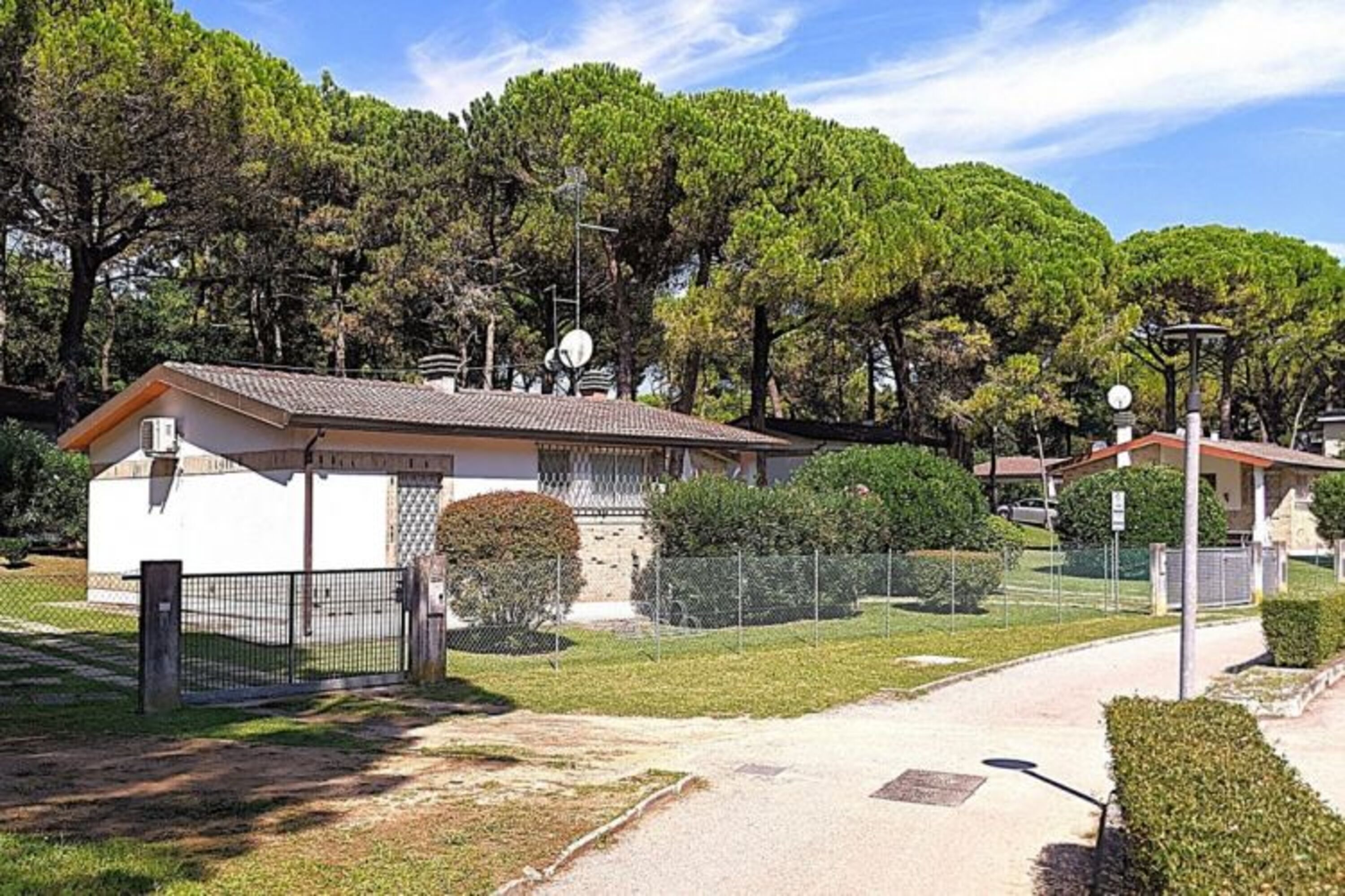 Una zona residencial con entrada vigilada, un pequeño edificio de techo con tejas y un camino que lleva a una casa.
