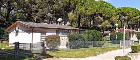Una zona residencial con entrada vigilada, un pequeño edificio de techo con tejas y un camino que lleva a una casa.
