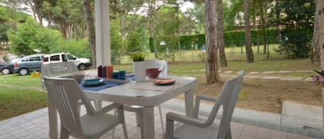 A patio area with a table and chairs, surrounded by trees and a parked car.
