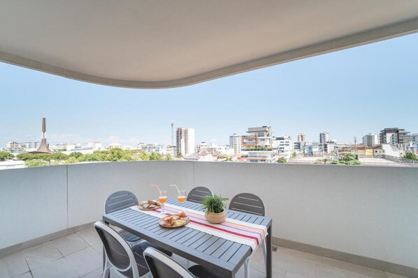 A balcony with a table set for two, featuring a city view, a plant, and a bottle of orange juice.