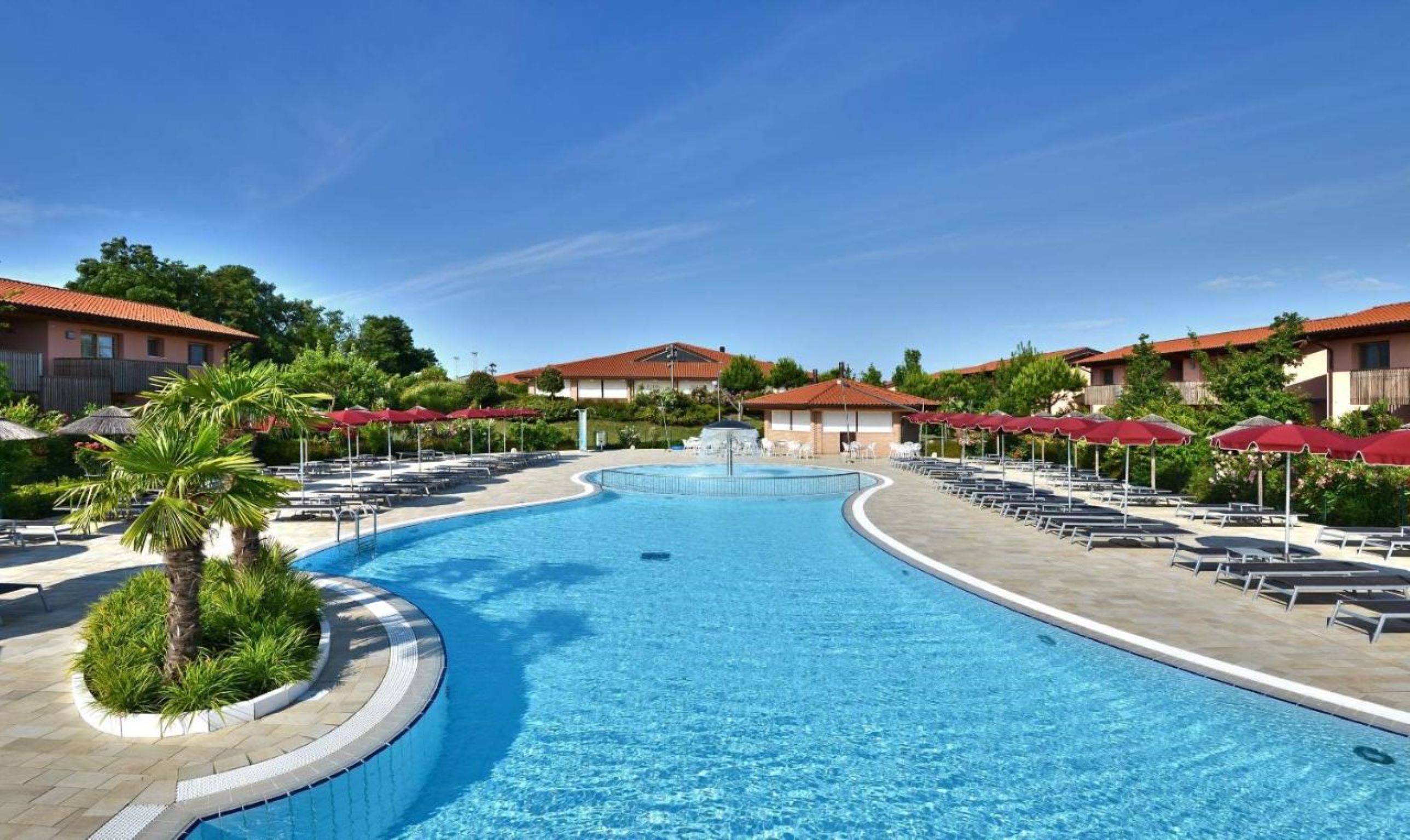 Ein Pool mit Liegestühlen und Sonnenschirmen, umgeben von Gebäuden mit roten Dächern.