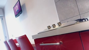 A kitchen with a red cabinet, a stainless steel stove, and a wall-mounted television. - Stylish studio with outdoor pool (Bibione)