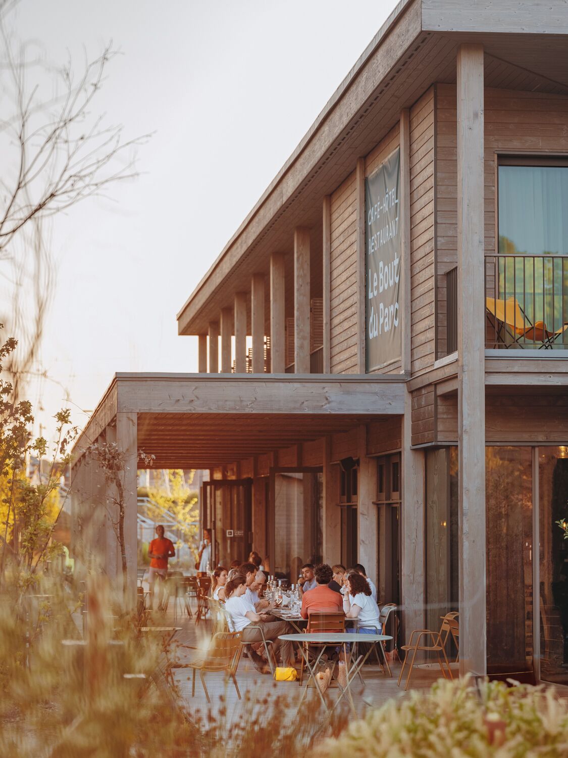 Un espace extérieur aménagé avec des tables et des chaises, une façade en bois et une enseigne indiquant « Le Bout du Parc ».