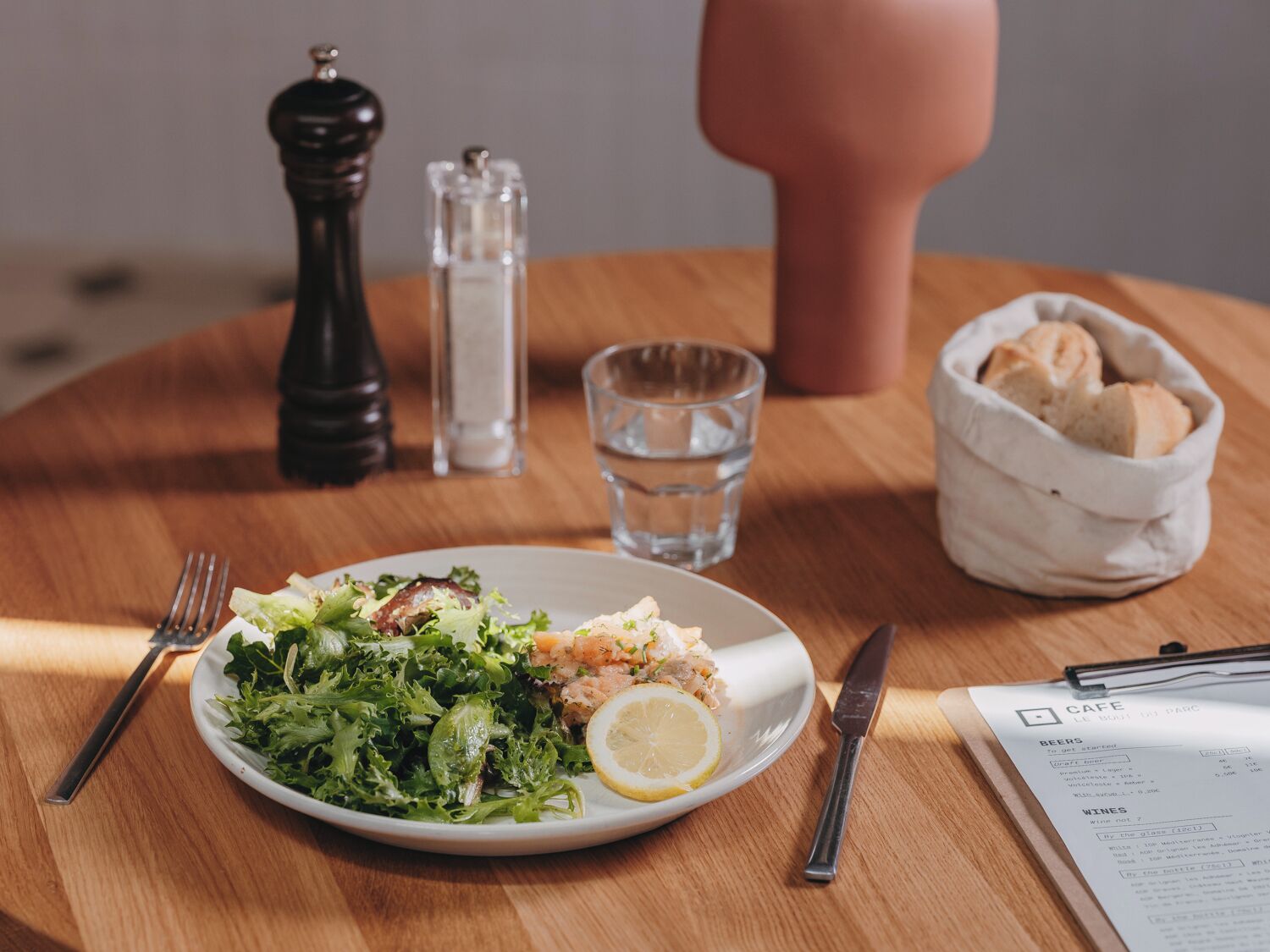 A table with a plate of food, a glass of water, a salt shaker, a pepper shaker, a bread basket, and a menu.