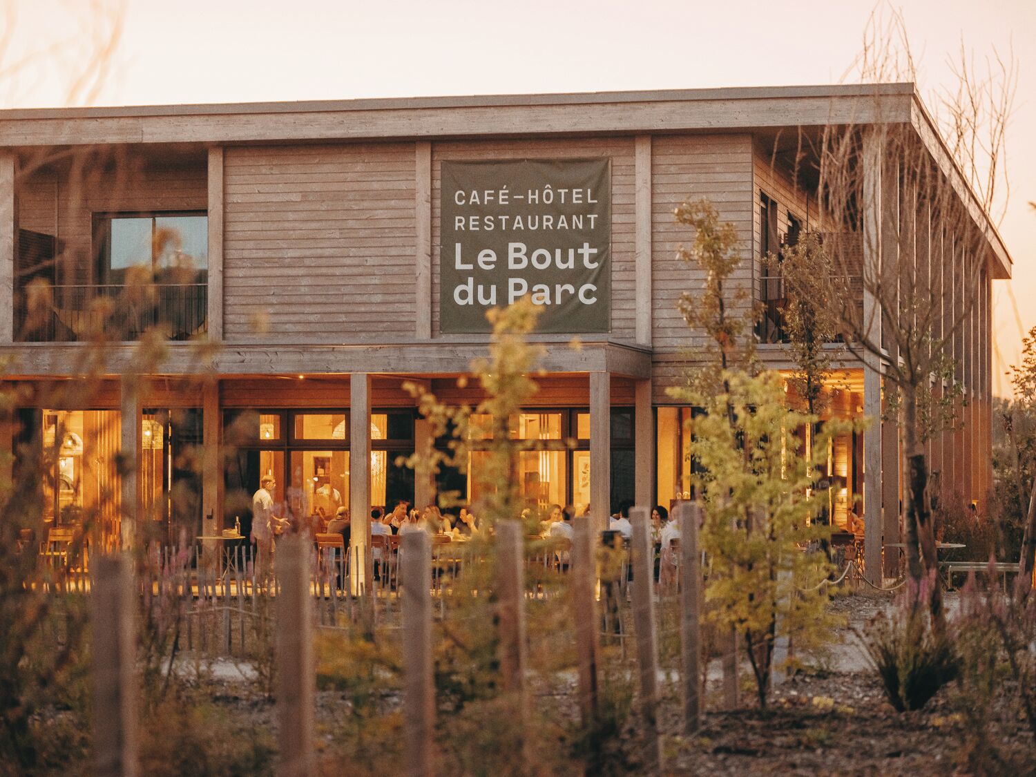 Een café-hotel-restaurant genaamd Le Bout du Parc, met een houten gevel en zichtbare terrasplekken.