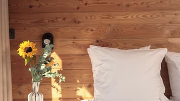 Puinen seinä, valkoisilla lakanoilla pedattu sänky, pienellä pöydällä oleva kamera ja auringonkukkia sisältävä maljakko.