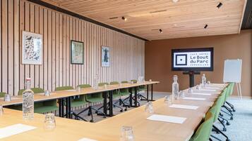 A conference room with a long table, green chairs, a whiteboard, and a projector screen displaying 'Le Bout du Parc'.