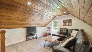 Un acogedor dormitorio en el ático con techo de madera, un sofá de cuero negro, un televisor y un letrero que dice 'palomitas de maíz'.