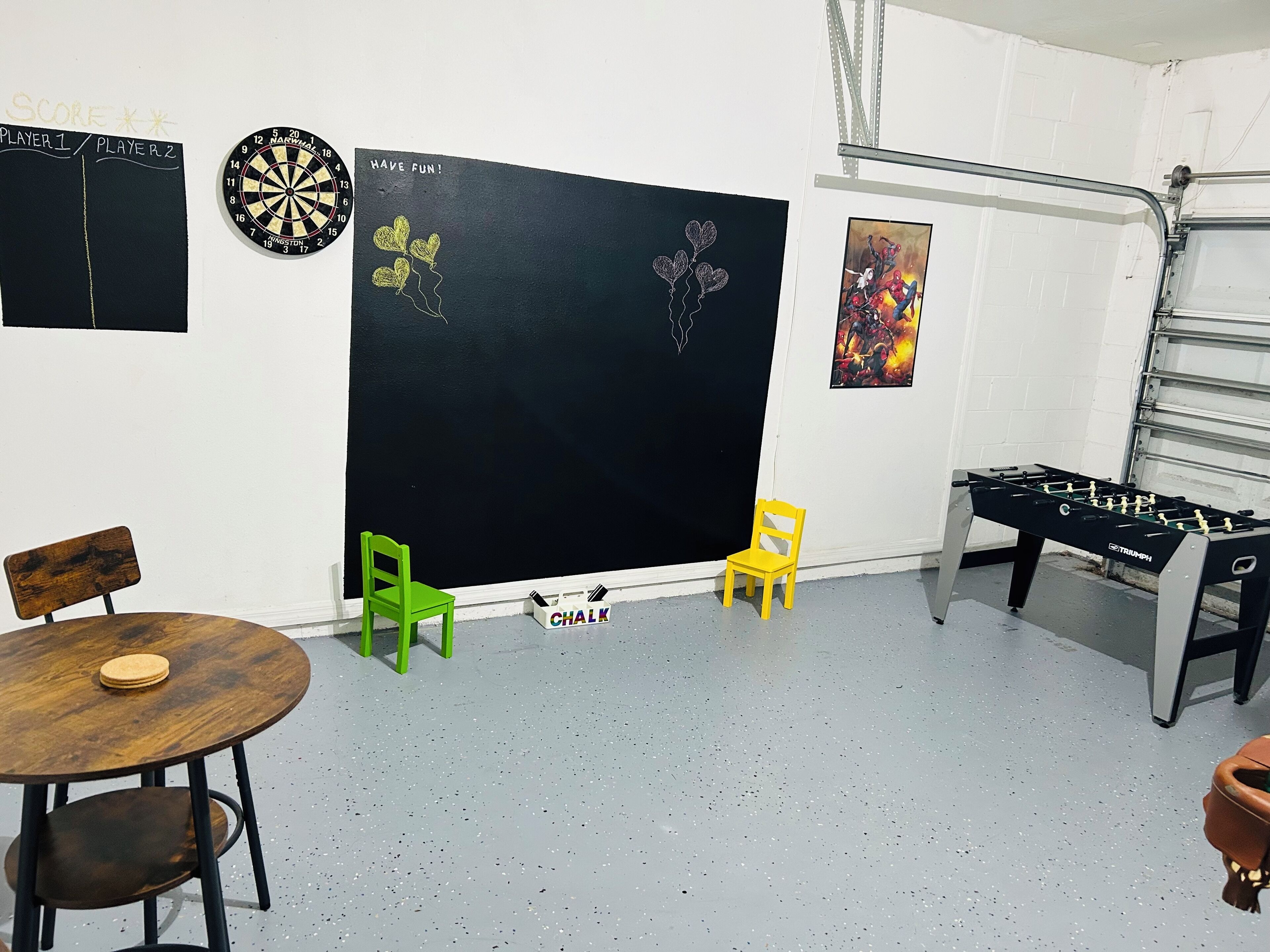 Een kamer met een dartbord, een prikbord, een tafelvoetbalspel en twee stoelen.