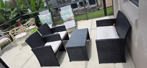 Een terras met rieten meubels, waaronder stoelen en een bank, en een kleine tafel.
