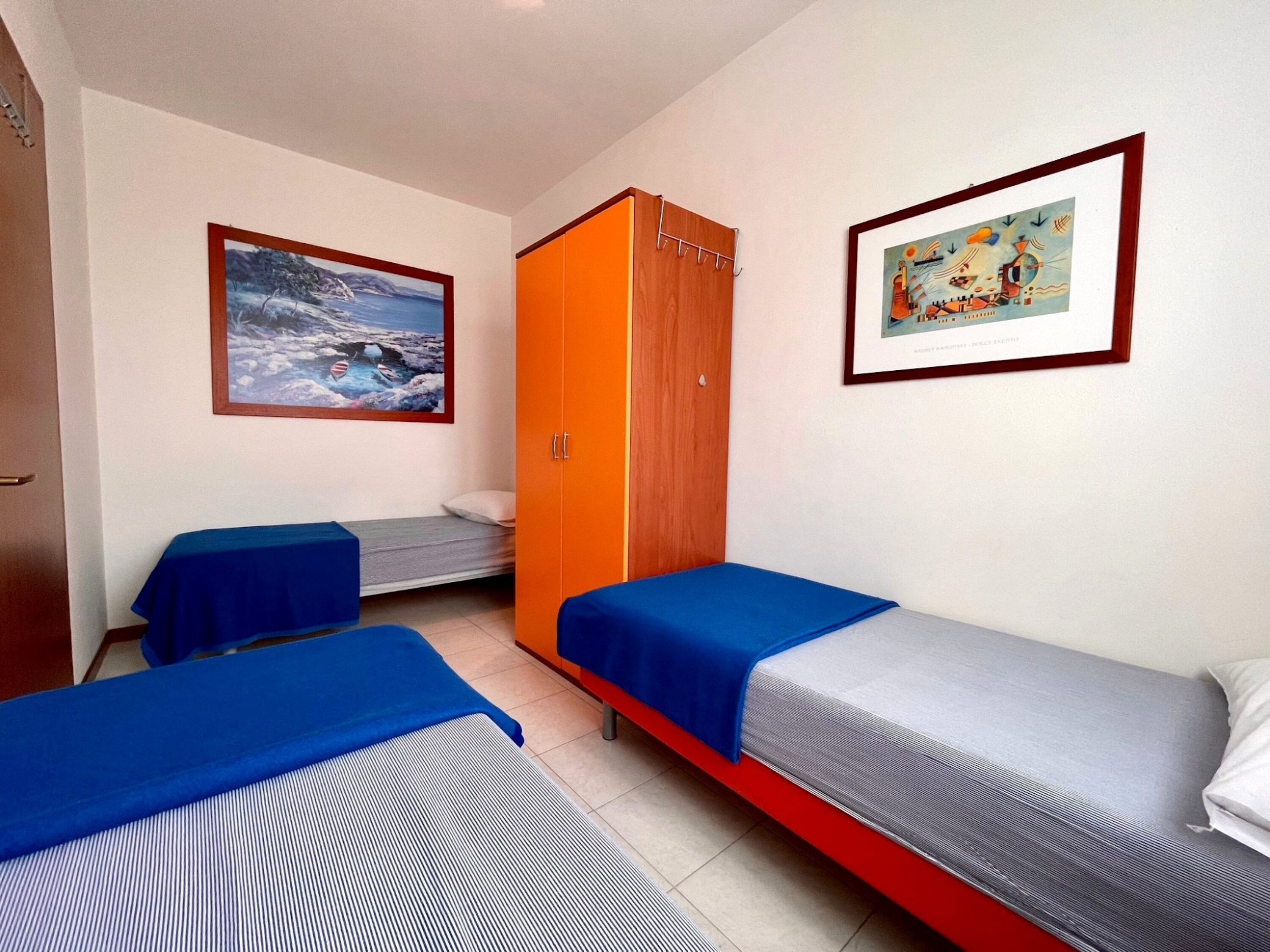 A room with two single beds, a wooden wardrobe, and two framed pictures on the walls.