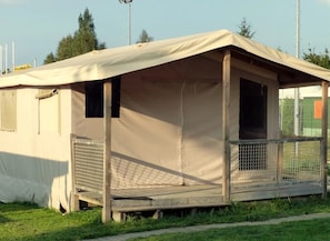 A small, single-story, beige tent-like structure with a covered porch and a fenced area.
