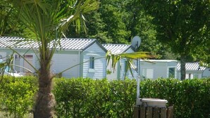 A row of mobile homes with a palm tree and a flower pot in the foreground. - Camping 3 étoiles - Piscine  - eeefba (Verteillac)
