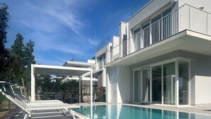 A modern house with a swimming pool, outdoor seating, and a covered patio area. - Stunning villa with pool and lagoon view (Isola di Albarella)