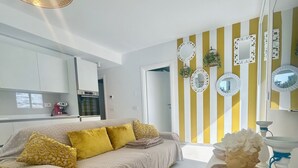 A modern living room with a sofa, a coffee table, and a kitchen area in the background. - Stunning villa with pool and lagoon view (Isola di Albarella)