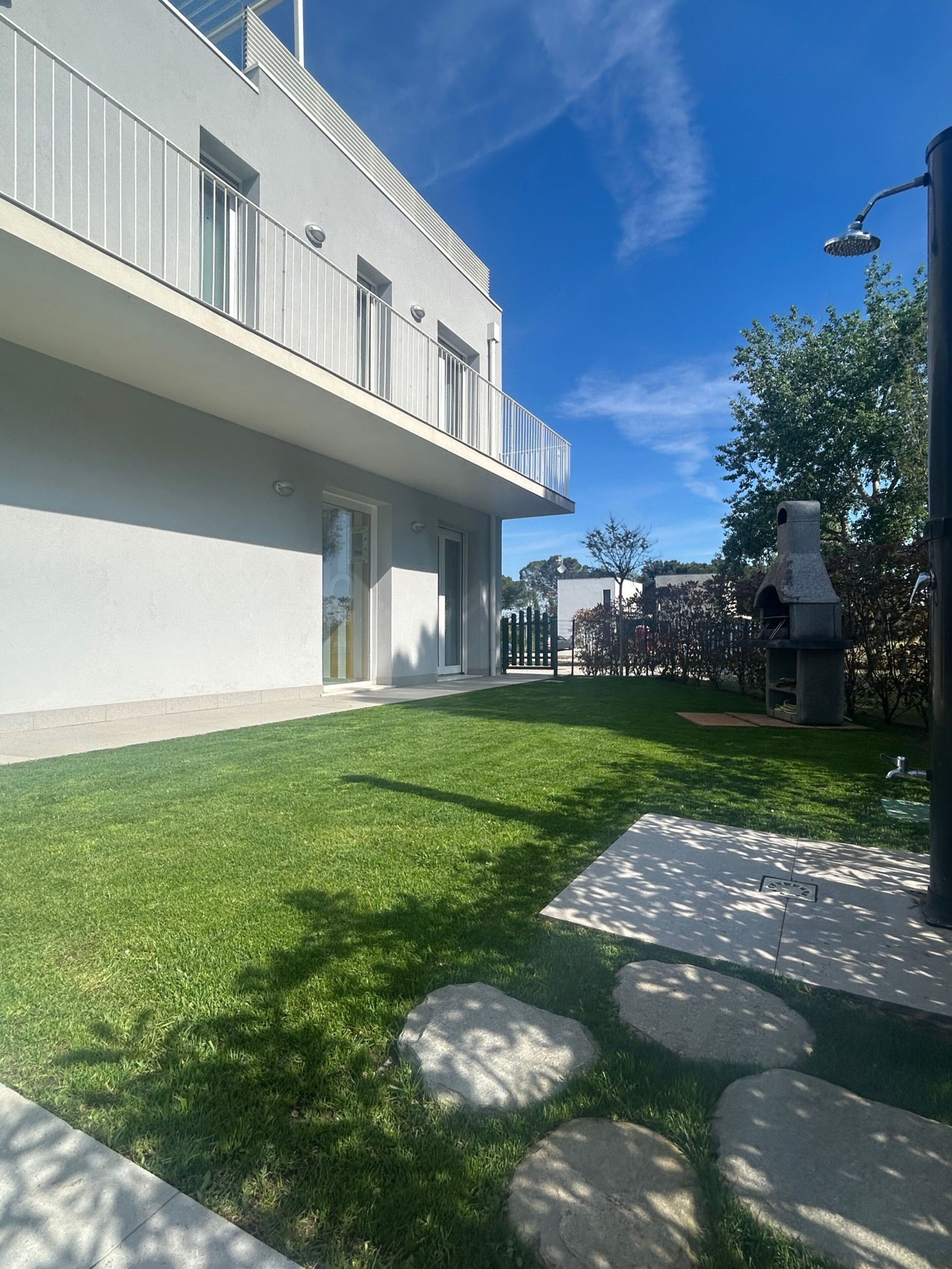 A modern building with a flat facade, a balcony, and a well-maintained lawn with stepping stones.