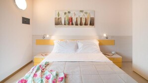 A bedroom with a bed, a nightstand, a bedside table, a painting on the wall, and a ceiling light.
