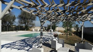 A covered outdoor seating area with white wicker furniture, a pool, and a pergola structure. - Serradei House (Torchiarolo)