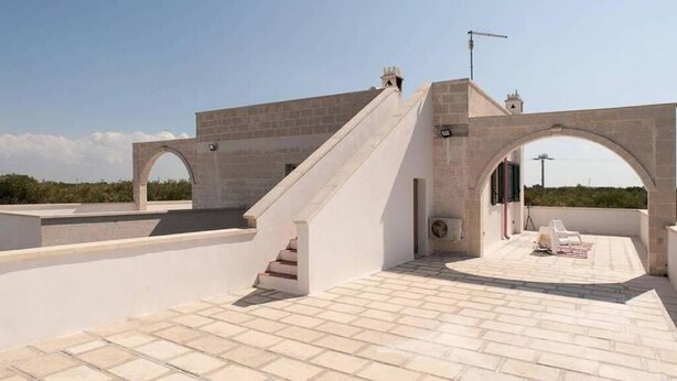 A rooftop terrace with stone flooring, a staircase, and a seating area with a table and chairs. - Serradei House (Torchiarolo)