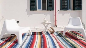 A room with two white plastic chairs, a small table with a bottle and glass, and a colorful striped rug. - Serradei House (Torchiarolo)