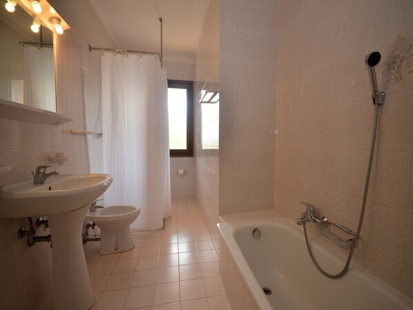 Une salle de bain équipée d’un lavabo, de toilettes et d’une baignoire. Une fenêtre laisse entrer la lumière naturelle.