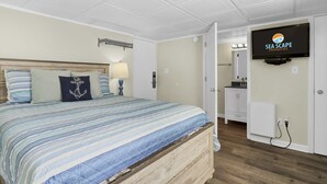 Un dormitorio con cama, televisión, baño y piso de madera.